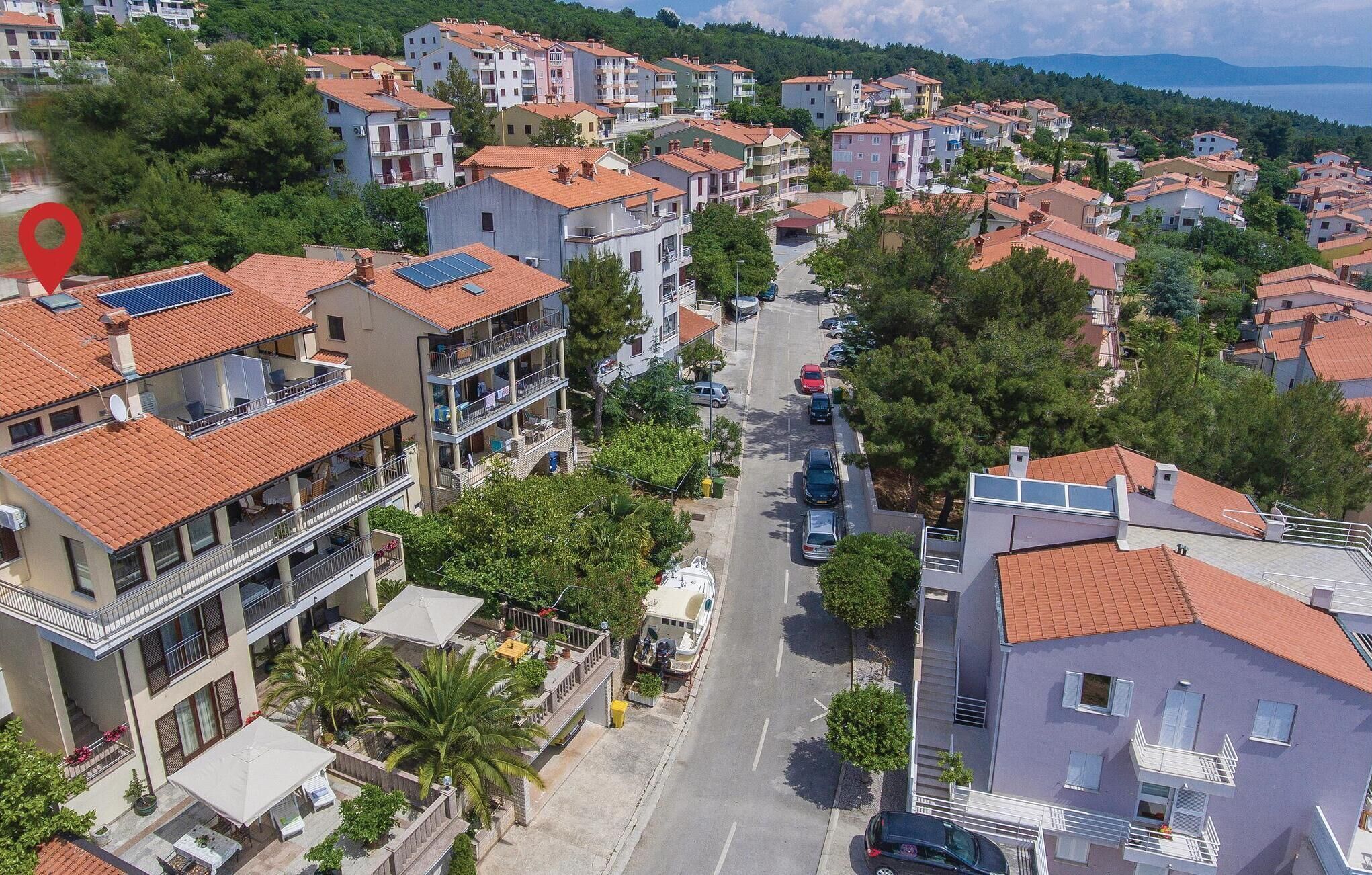 A residential area with multi-story buildings, a street with parked cars, and a body of water in the background.