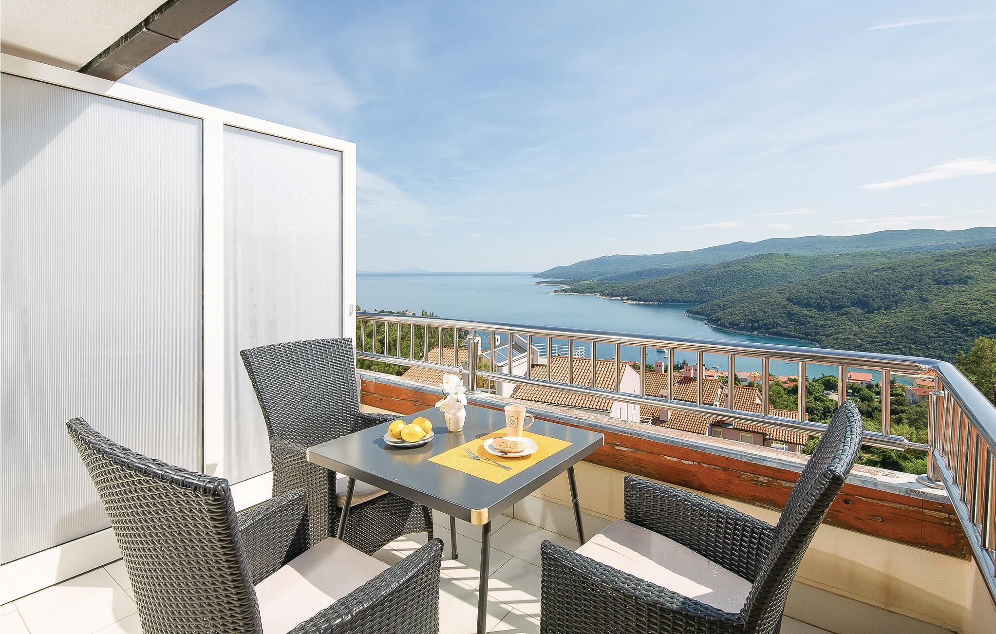 En balkong med möbler i rotting, ett bord med en tallrik full av citroner och en utsikt över en sjö och kullar.