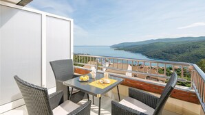 Un balcón con mobiliario de mimbre, una mesa con un plato de limones y vistas a un lago y colinas.