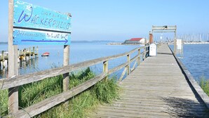 A wooden pier leading to a waterfront area with a sign indicating a cafe, bar, and bistro. - Garden Apartment 3 - Ferienhof Schmeling (Ahneby)