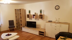 Una sala de estar con televisor, muebles de madera, una estantería y un reloj en la pared.