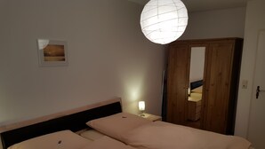 Un dormitorio con dos camas individuales, un armario de madera, una lámpara de noche y un cuadro en la pared.