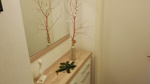 Un baño con tocador de madera, un espejo, un florero con ramas y un adorno pequeño.