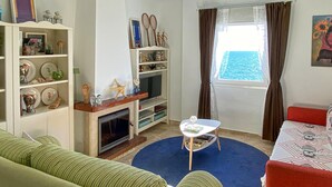 A living room with a fireplace, a television, a sofa, a coffee table, and a view of the sea through a window. - 1 bedroom beach front apartment in Mezquitilla (Mezquitilla)