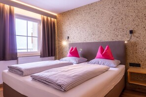 A hotel room with two beds, a window with curtains, a textured wall, and a bedside table.