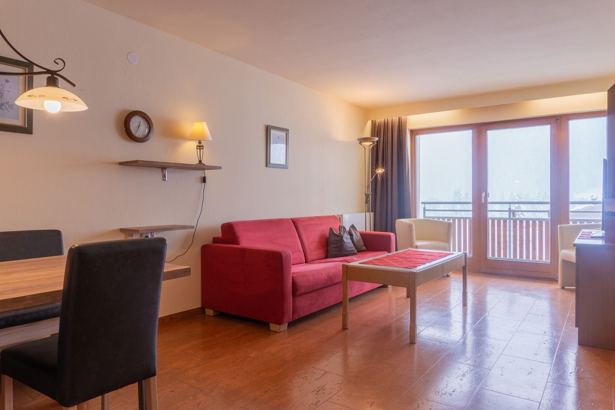 Ein Wohnzimmer mit rotem Sofa, einem Holztisch und einem Balkon mit Aussicht.