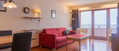 Una sala de estar con un sofá rojo, una mesa de madera y un balcón con vistas.