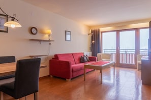 A living room with a red sofa, a wooden table, and a balcony with a view.