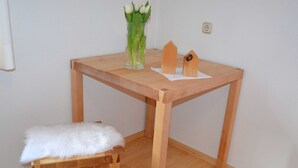 A wooden table with a vase of flowers, a white fluffy cushion, and two wooden objects on a white wall. - Holiday at Rüf's - Apartment 1 (2-6 people) (Au)