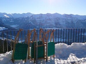 Une vue sur une montagne enneigée, avec une rambarde et deux chaises vertes.