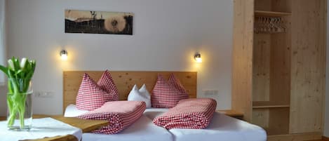 A wooden bed with checkered bedding, a wall-mounted light, and a wooden cabinet with shelves.