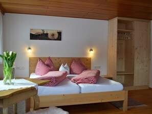 A wooden bed with checkered bedding, a wall-mounted light, and a wooden cabinet with shelves. - Holiday at Rüf's - Apartment 1 (2-6 people) (Au)