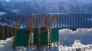 A snow-covered mountain view with a railing and two green chairs. - Holiday at Rüf's - Apartment 1 (2-6 people) (Au)