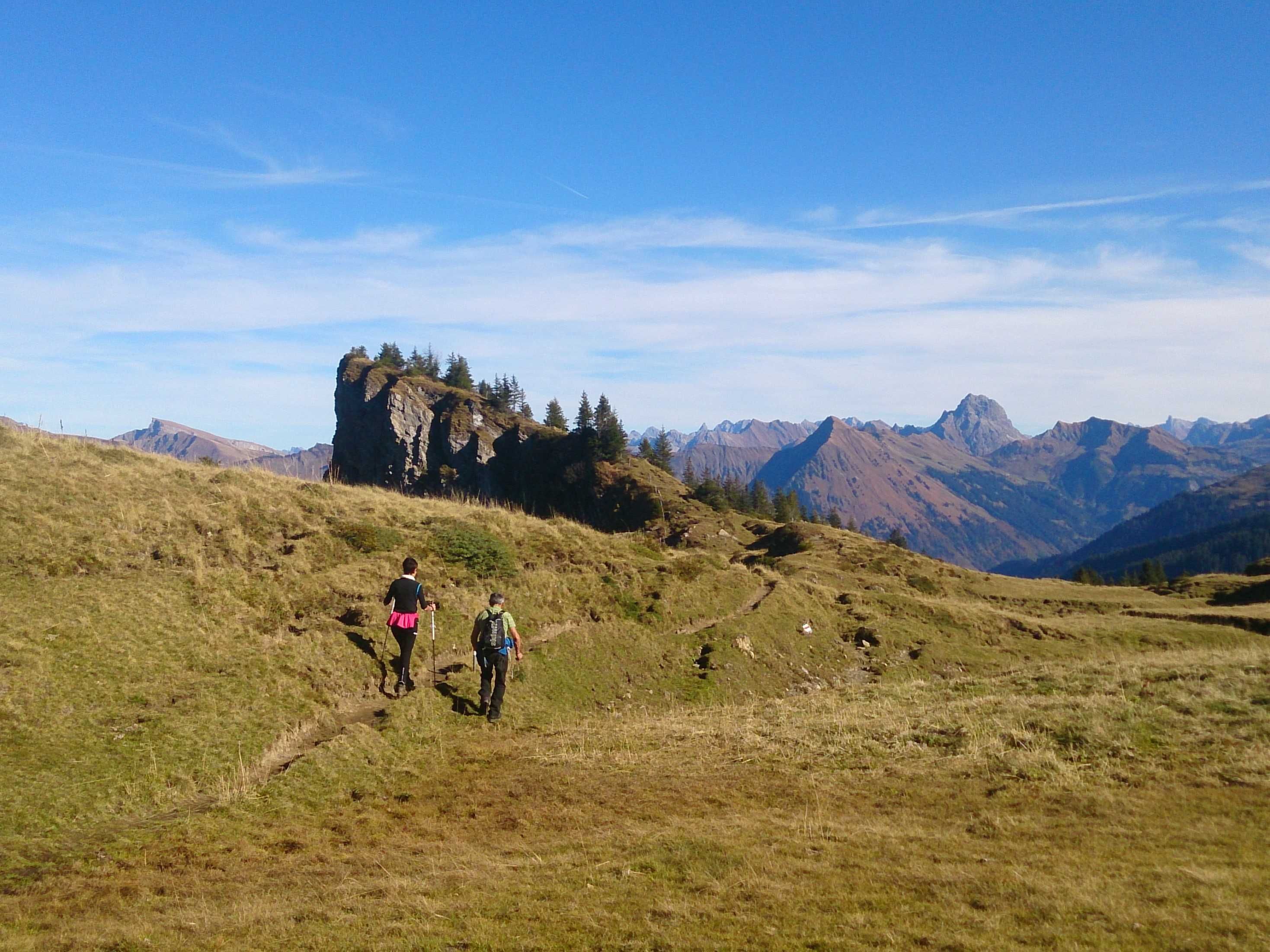 Un sentier de randonnée dans une région montagneuse, parsemée d’affleurements rocheux et offrant une vue sur des sommets lointains.
