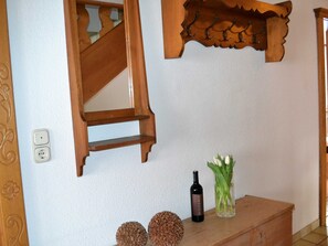 Un escalier en bois avec une rampe décorative, un interrupteur fixé au mur, une bouteille de vin et un vase rempli de fleurs, le tout posé sur un meuble en bois.