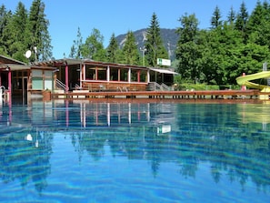 A pool area with a wooden building, a lifeguard stand, and a mountain backdrop. - Holiday at Rüf's - Apartment 1 (2-6 people) (Au)