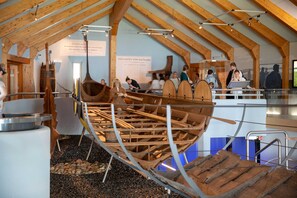 Eine Museumsausstellung mit einem großen hölzernen Bootsmodell, Informationstafeln und Besuchern.