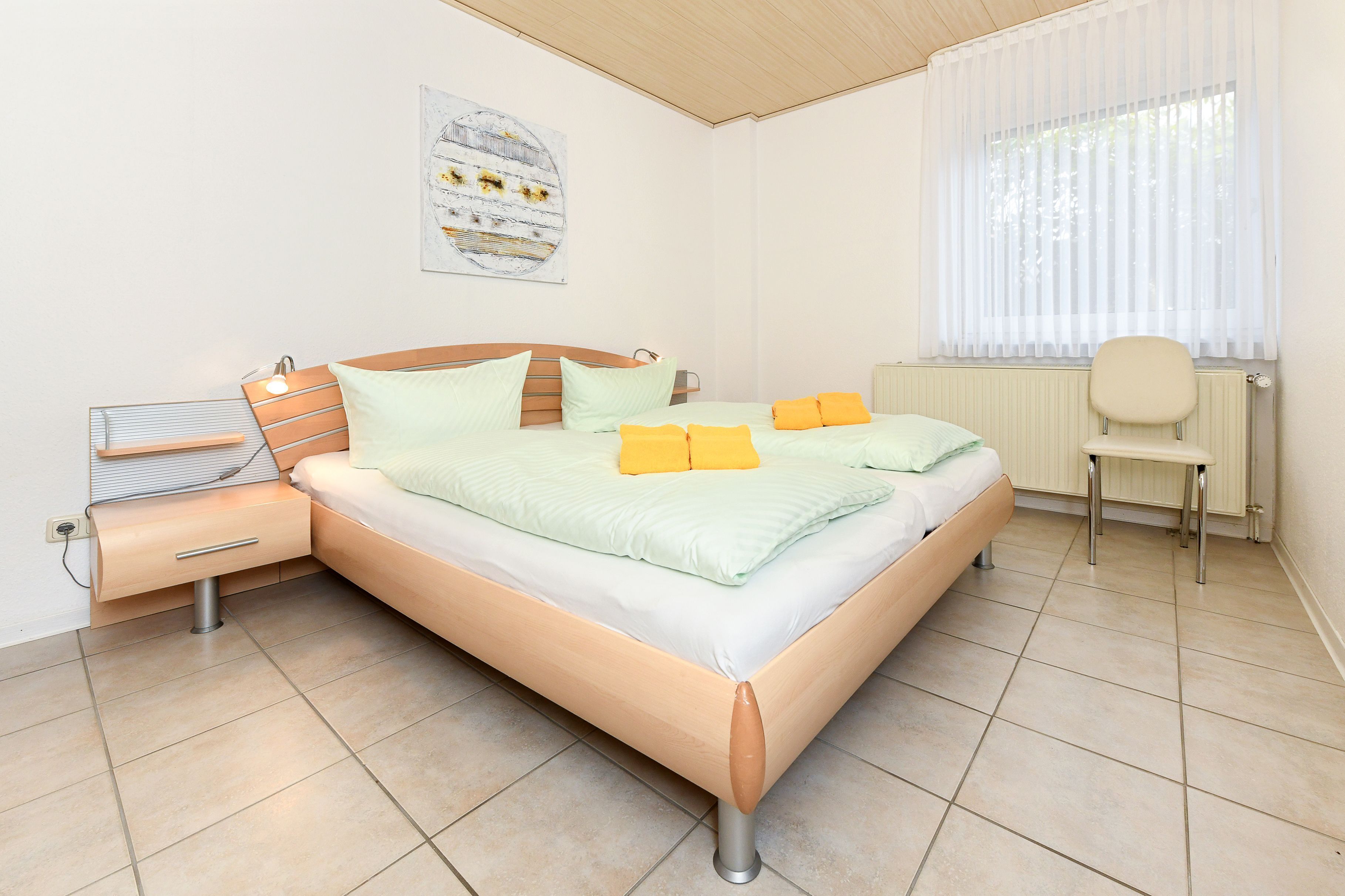 A bedroom with a bed, bedside table, chair, and a window with curtains.