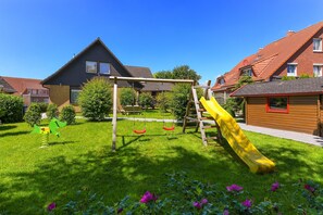 Zona residencial amb un parc infantil, incloent balançs i tobogan, envoltada de cases amb teulades vermelles.