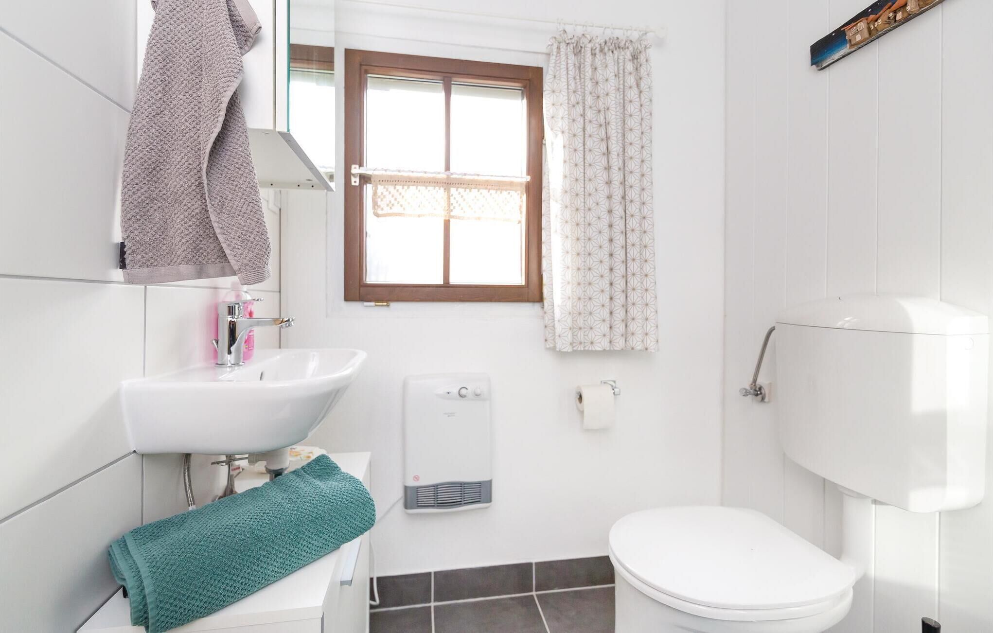 A bathroom with a white sink, a toilet, and a window with patterned curtains.