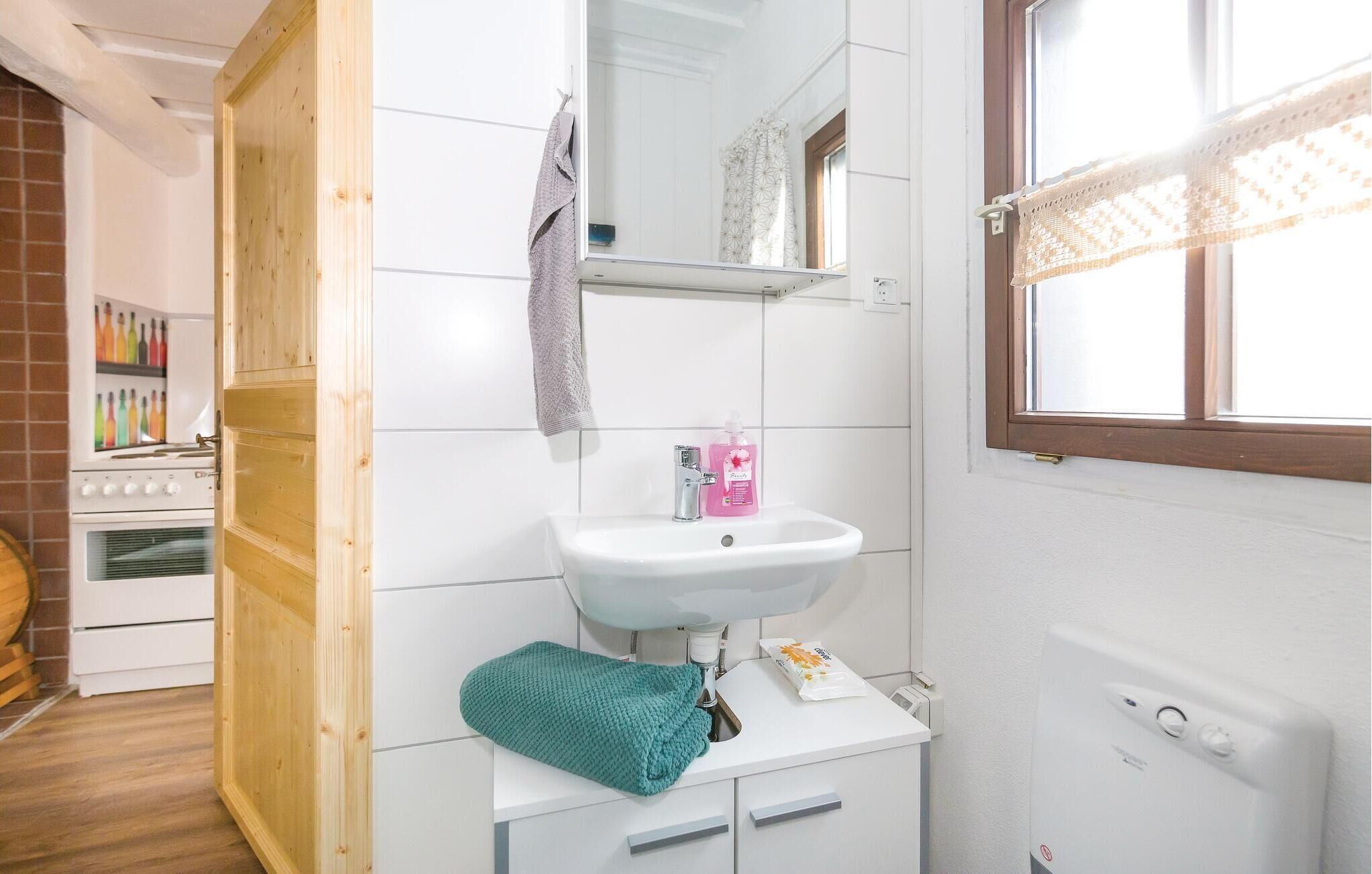 Une salle de bain avec un lavabo blanc, un miroir, un porte-serviettes, une fenêtre avec des rideaux en dentelle et un élément chauffant visible.