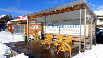 Een overdekt terras met houten stoelen, een houten gebouw met een bord en sneeuw op de grond.