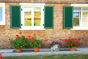 Un edificio con revestimiento de madera, contraventanas verdes y macetas con flores rojas.