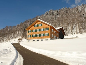 Un edificio de varios pisos con techo inclinado, rodeado de árboles cubiertos de nieve y un cielo despejado.