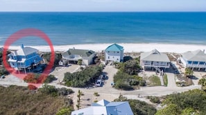 Une propriété située sur la côte, comprenant plusieurs maisons, une plage de sable et l’océan en toile de fond.