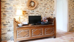 Un muro de piedra con un televisor sobre un mueble de madera, una lámpara y una radio.