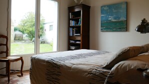 Un dormitorio con cama, una silla de madera, una estantería y un cuadro de una vista marina.
