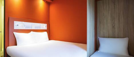 Habitación de hotel con una cama grande, cabecera de madera y una lámpara fijada a la pared.