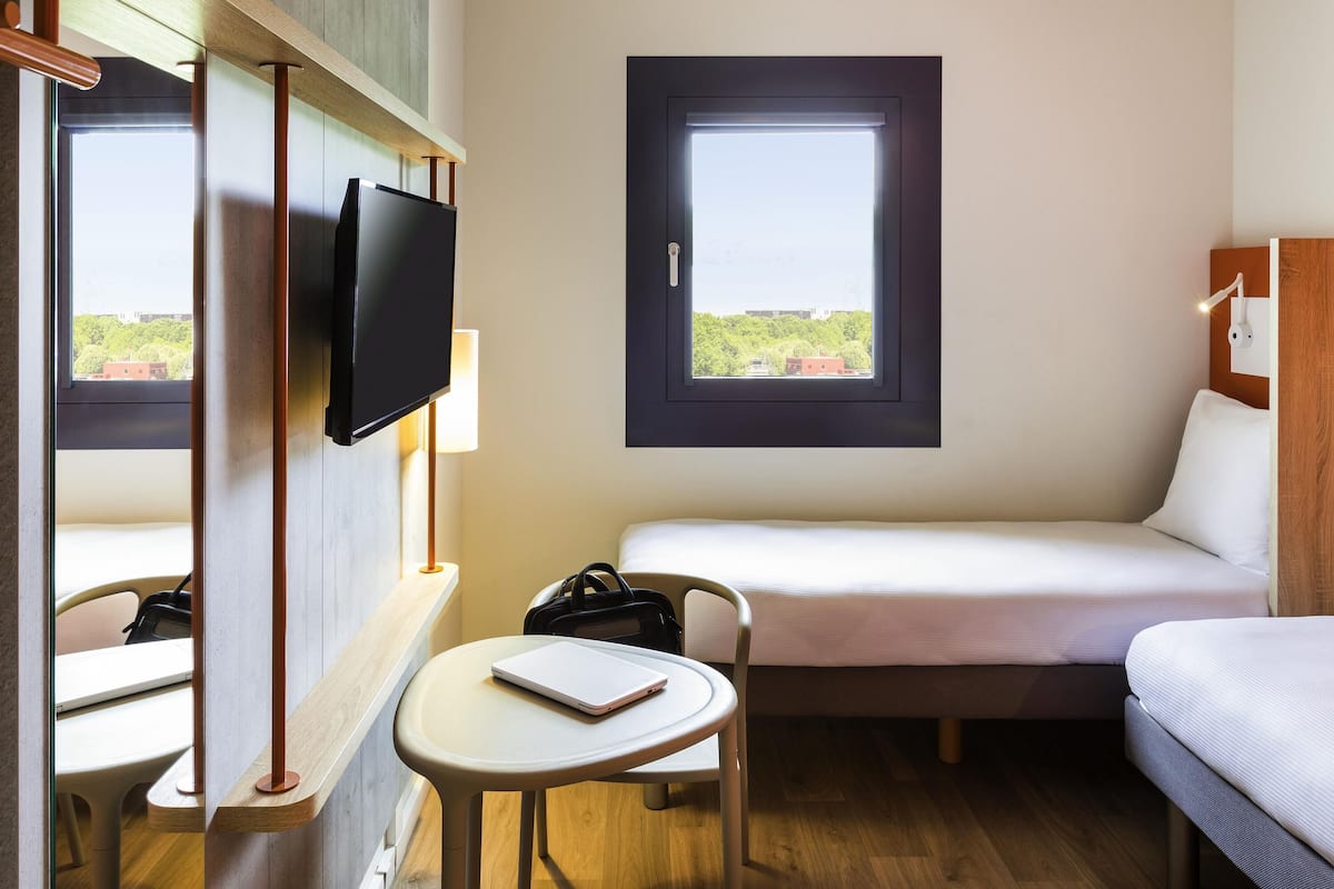 A hotel room with a bed, a desk with a laptop, a TV, and a window with a view.