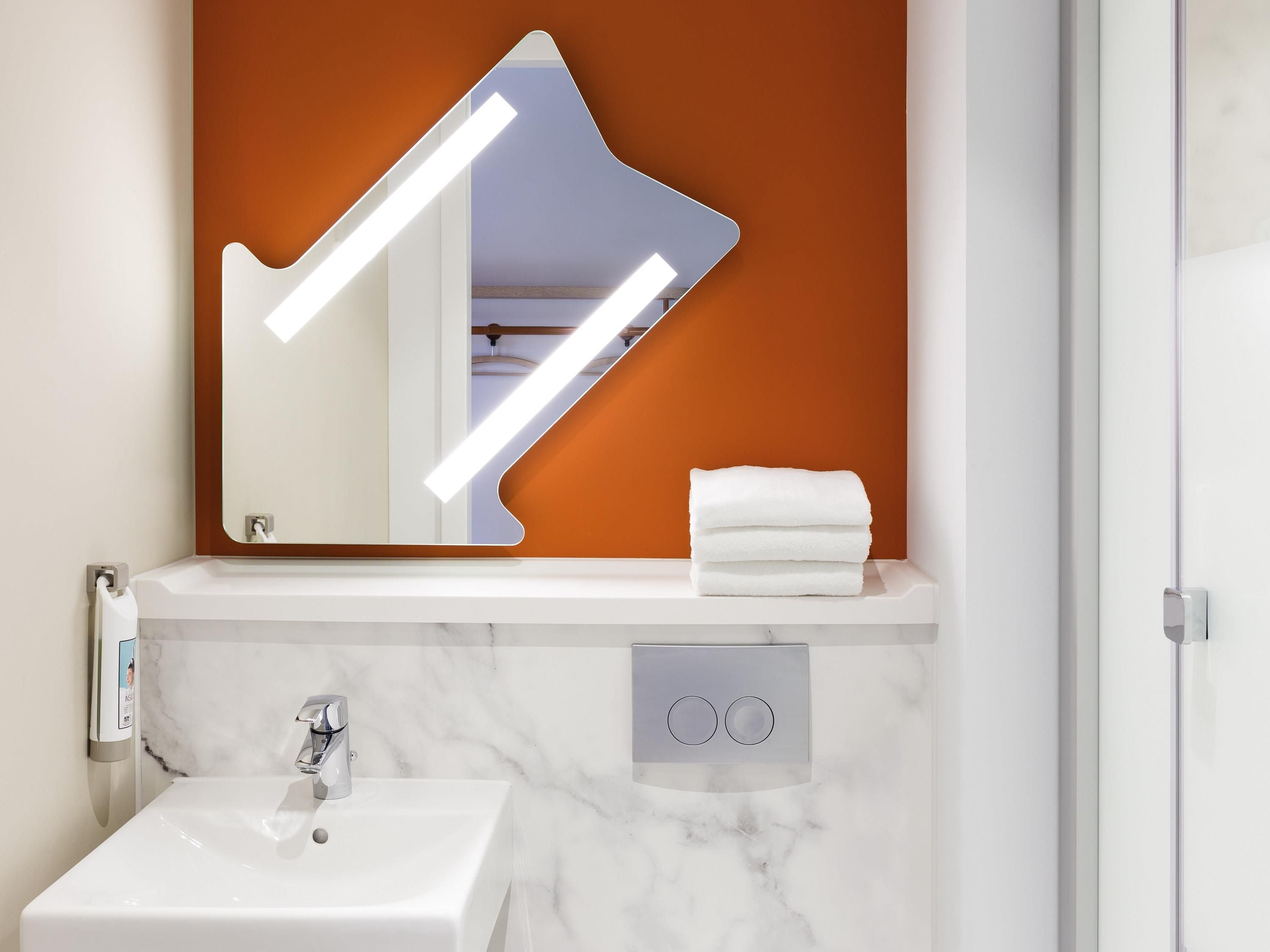 A bathroom with a white sink, a mirror with lights, and a towel on the counter.