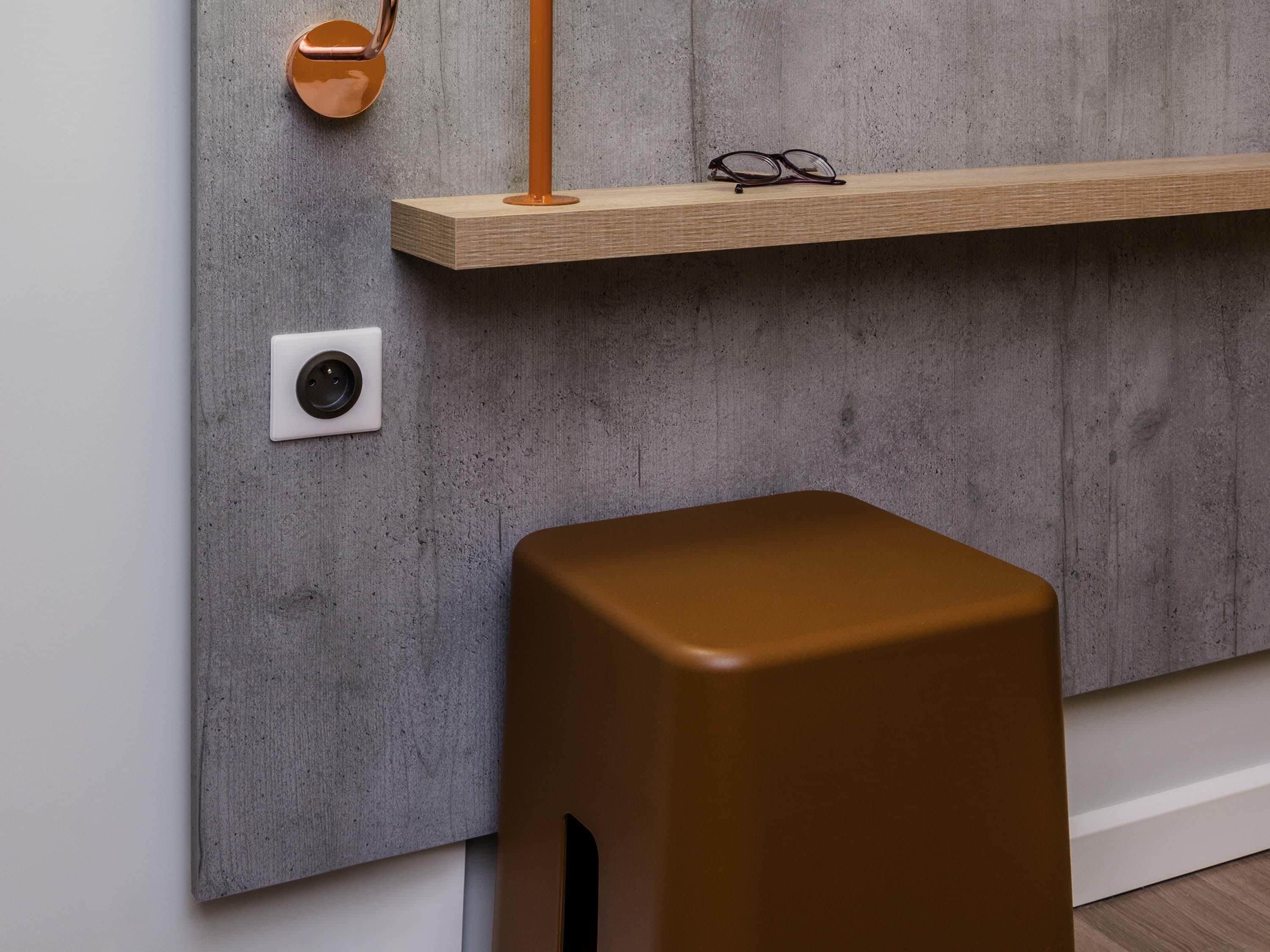 A modern interior with a concrete wall, a wooden shelf, a pair of glasses, and a brown stool.