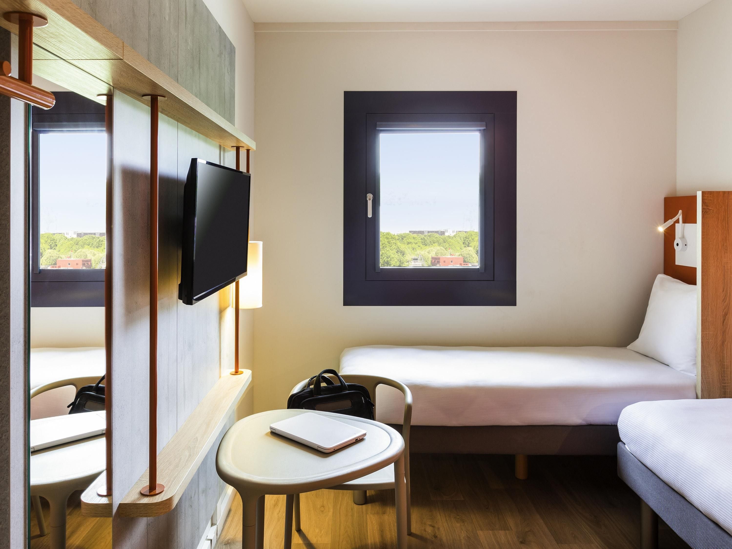 Een hotelkamer met een bed, een bureau met een laptop, een televisie en een raam met uitzicht.