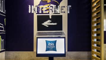 A workspace with a laptop, keyboard, and mouse on a wooden desk, a computer monitor displaying 'ibis budget hotels,' and a wall with a large 'INTERNET' sign and an arrow pointing left.