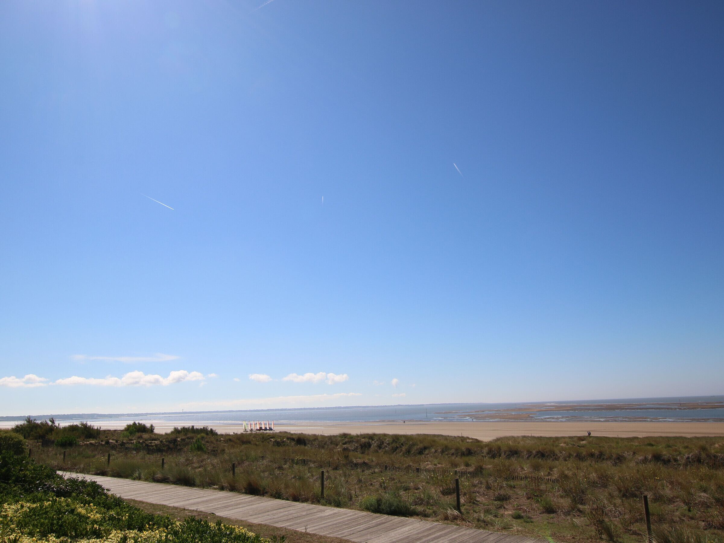 A wooden boardwalk leading to a beach with a clear sky and distant dunes.