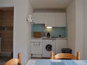 Ett kompakt kök med vita skåp, en kaffebryggare, en brödrost och en tvättmaskin.