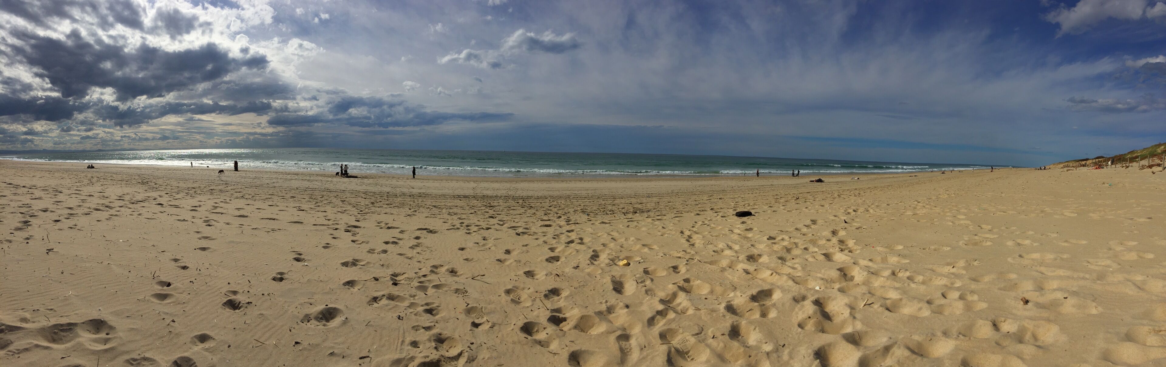A wide sandy beach with footprints and a few people in the distance.
