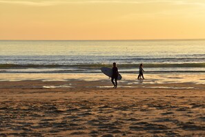 A beach scene with two people walking along the shore, one carrying a surfboard. - Fully renovated 4-person apartment 2 minutes from the beach (Seignosse)
