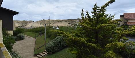 Un chemin menant à un bâtiment d’où l’on peut admirer une colline, ainsi qu’à un parking où sont garées des voitures.
