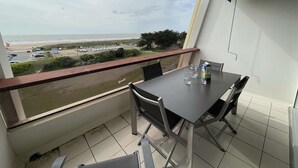 Ein Balkon mit Tisch und Stühlen mit Blick auf einen Strand und einen Parkplatz.