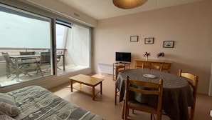Ein Zimmer mit einer Couch, einem Esstisch mit Stühlen, einem Fernseher und einem großen Fenster.