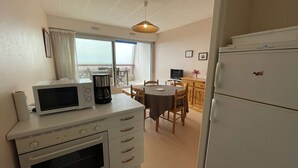 Eine kompakte Küche mit Mikrowelle, Kaffeemaschine, Backofen und Kühlschrank. Es gibt einen Essbereich mit Tisch und Stühlen sowie ein Fenster mit Blick.