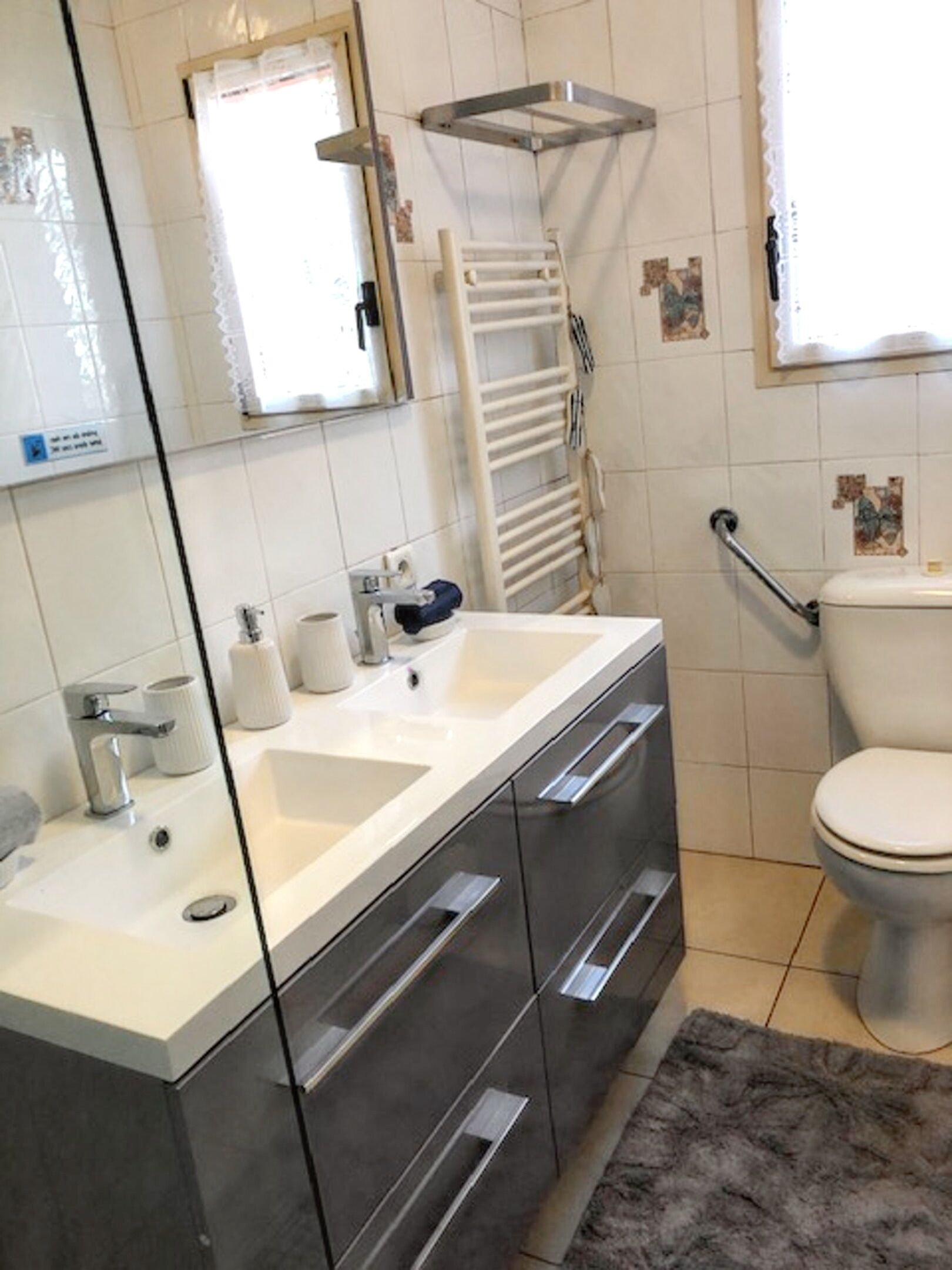 Un baño con lavamanos blanco, espejo y retrete. Hay un perchero y una alcachofa de ducha en la pared.