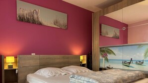 A hotel room with a bed, two bedside tables with lamps, a large mirror, and two wall-mounted paintings.