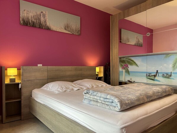 A hotel room with a bed, two bedside tables with lamps, a large mirror, and two wall-mounted paintings.