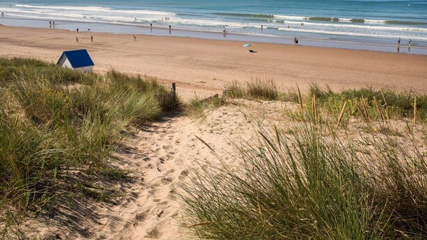 A beach with a dune path leading to a blue structure, likely a beach hut.