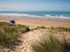 A beach with a dune path leading to a blue structure, likely a beach hut.